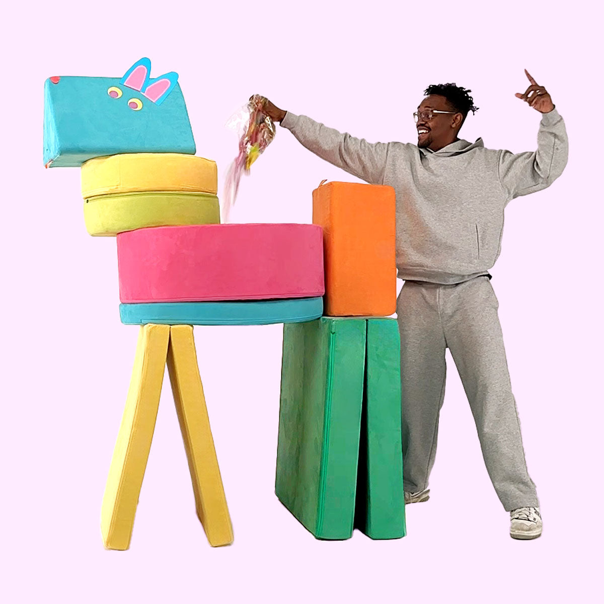 A man puts the finishing touches on a giant piñata built from colorful pieces of Nugget play couches and a Chunk play ottoman.