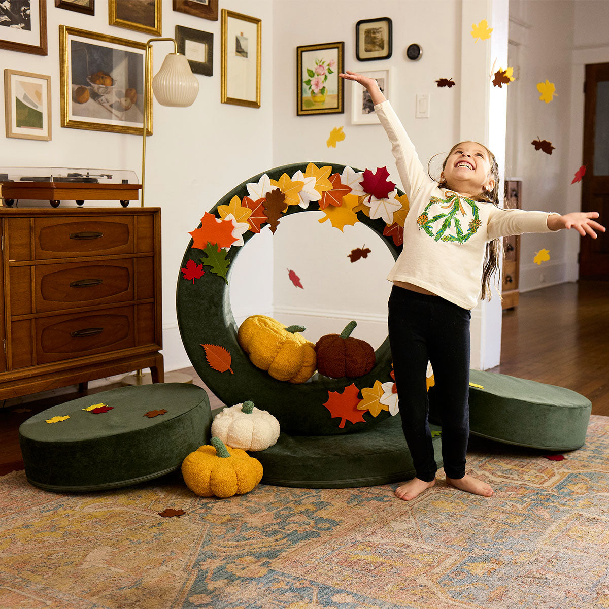 A child throws play leaves in the air alongside a Chunk play ottoman arranged as a cornucopia.
