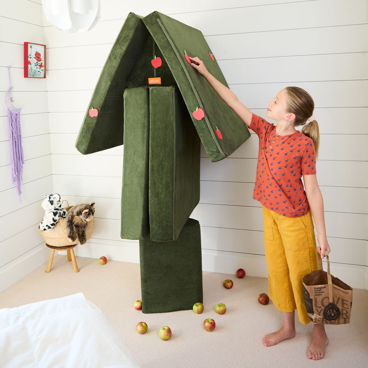 A child pretends to pick apples from a tree built from a Nugget play couch.