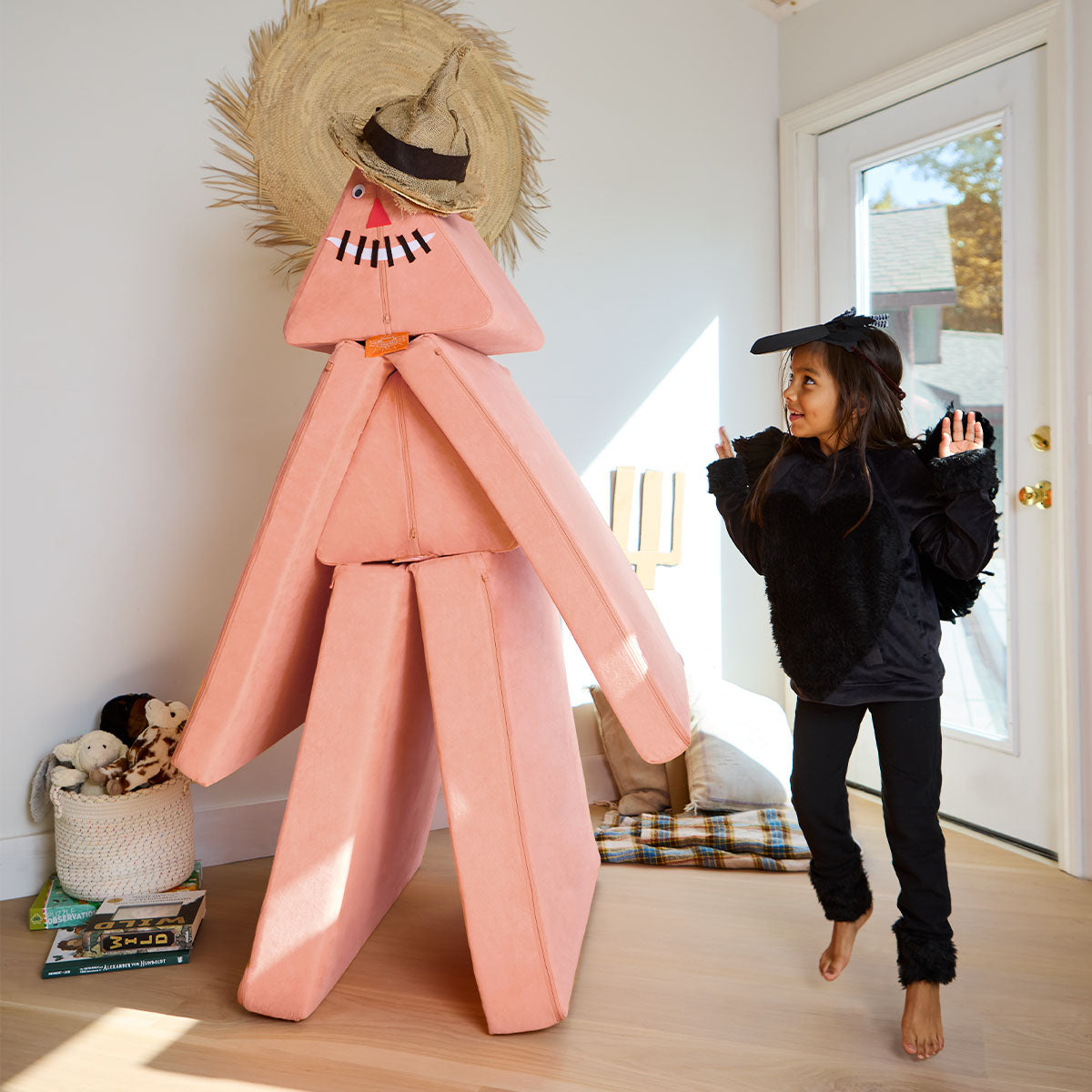 A child, dressed as a crow, runs around a scarecrow built from a Nugget play couch.