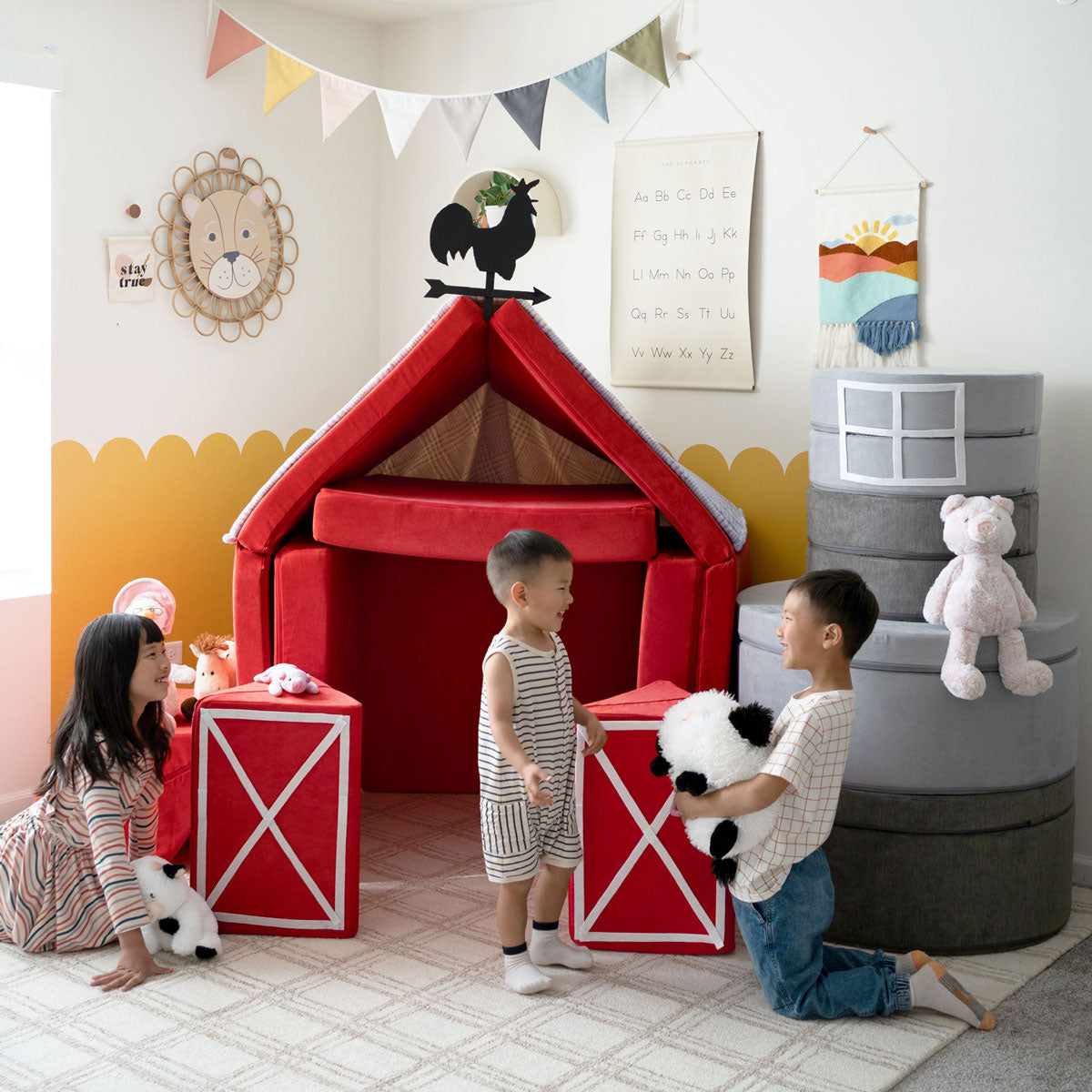 Three kids play around a pretend barn made from two red Nugget play couches.