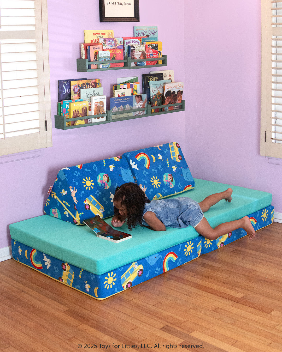 A child reads a book sprawled on a Ms. Rachel Nugget play couch, which is patterned with icons from popular Ms. Rachel songs.