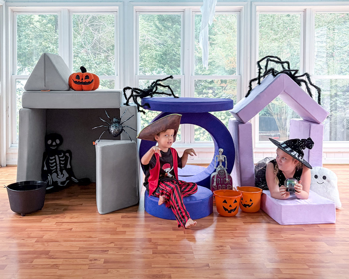 Two children in costume play amongst three forts made from a gray Nugget, indigo Chunk, and lilac Smore.