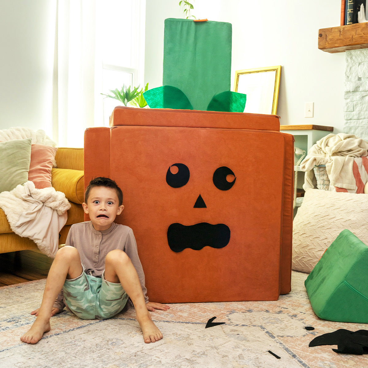 A child mimics the jack-o-lantern face on the side of a giant pumpkin build made from a Nugget.
