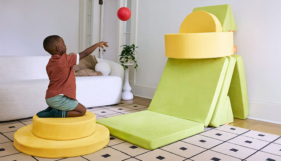 Photo shows a child tossing a ball into a basketball hoop build created from a yellow play ottoman and chartreuse play couch.