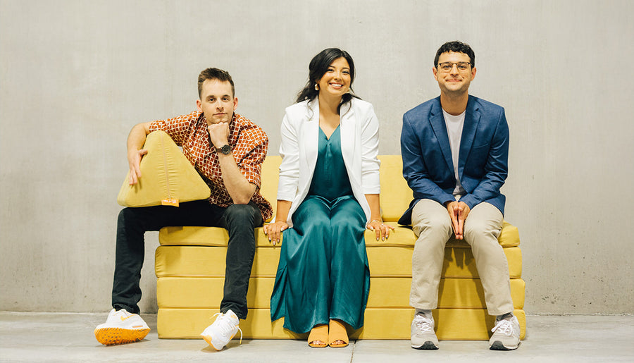 The three co-founders of Nugget Comfort, seated side by side on a yellow play couch.