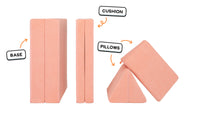 Four pieces of a light peach Nugget play couch lined up: one foldable base, one foldable cushion, and two triangular pillows.