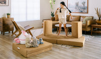 A child sings into a pretend mic to an audience of stuffies while standing on a Camelot camel brown play couch by Nugget.