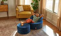 A child relaxes in a Blueridge navy blue Chunk play ottoman, set up in a chair configuration.