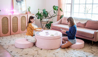 Two children play a card game on a Heartthrob blush pink Chunk play ottoman set up as a table and two chairs.