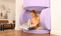 A child reads inside a Moonshot lilac purple Chunk play ottoman, set up as a small fort.