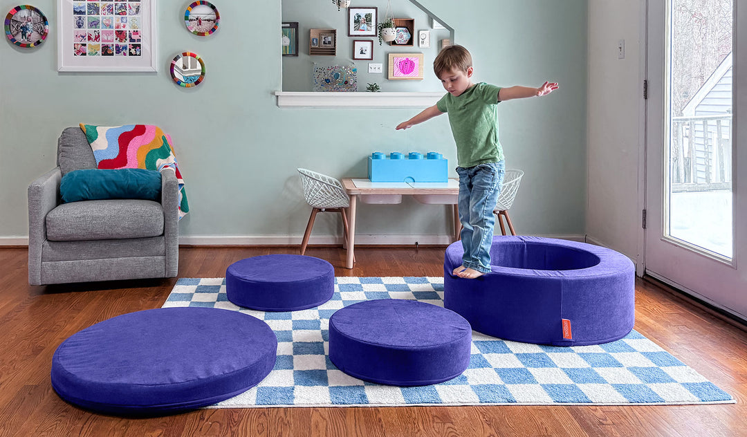 A child balances on the pieces of a Chunk play ottoman in Nebula vibrant indigo, set up as stepping stones.