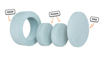 Four pieces of a light gray-blue Chunk play ottoman lined up: one large hoop, two sturdy nesting, and one wider pad for the lid.