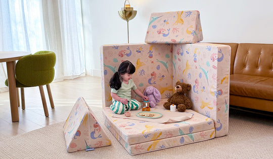 A young child hosts a pretend tea party on a unicorn-patterned Fable Nugget play couch.