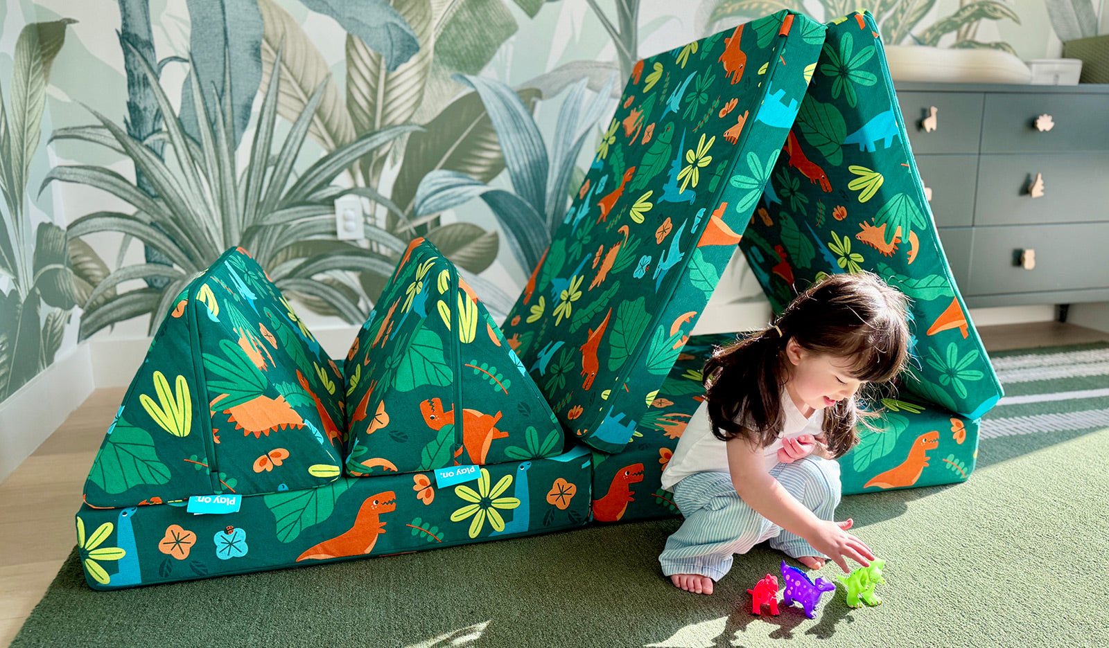 A young child plays with toy dinosaurs next to a dinosaur-patterned Fossil Nugget play couch.