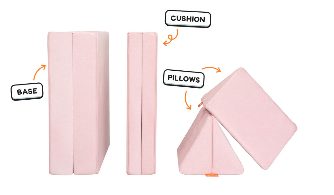 Four pieces of a blush pink Nugget play couch lined up: one foldable base, one foldable cushion, and two triangular pillows.
