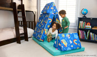 Two children play on the pieces of a vibrant Ms. Rachel-patterned Nugget play couch, set up as a tent and hurdle.