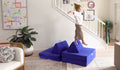 A child balances on one foot on top of a triangular pillow on an indigo play couch by Nugget.