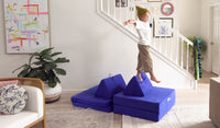 A child balances on one foot on top of a triangular pillow on an indigo play couch by Nugget.