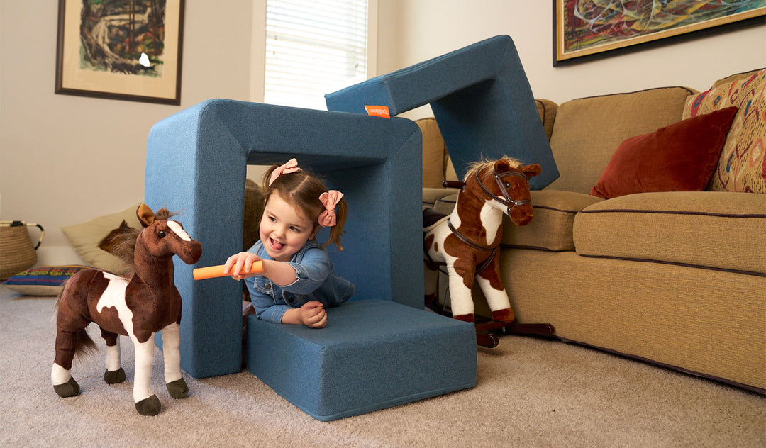 A child plays with toy horses in a makeshift barn made from the three pieces of a dark-wash denim play chair.