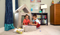 Two children put together a puzzle on the block of a beige Smore play chair, beside a small fort made of the other two Smore pieces.