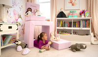 A child plays with dolls and stuffies inside the pieces of a blush pink Smore play chair.