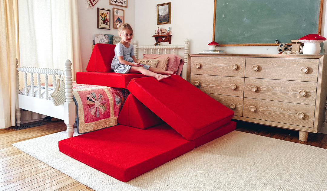 A child plays on an all-red play couch by Nugget, set up as a slide down from the child's bed.