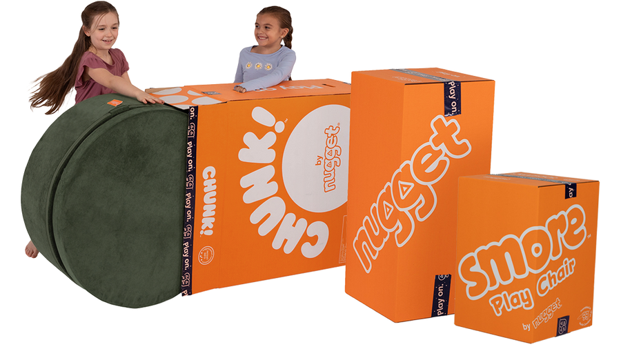 Two children roll a Chunk play ottoman from its Big Orange Box, alongside two other Big Orange Boxes of a Nugget play couch and Smore play chair.