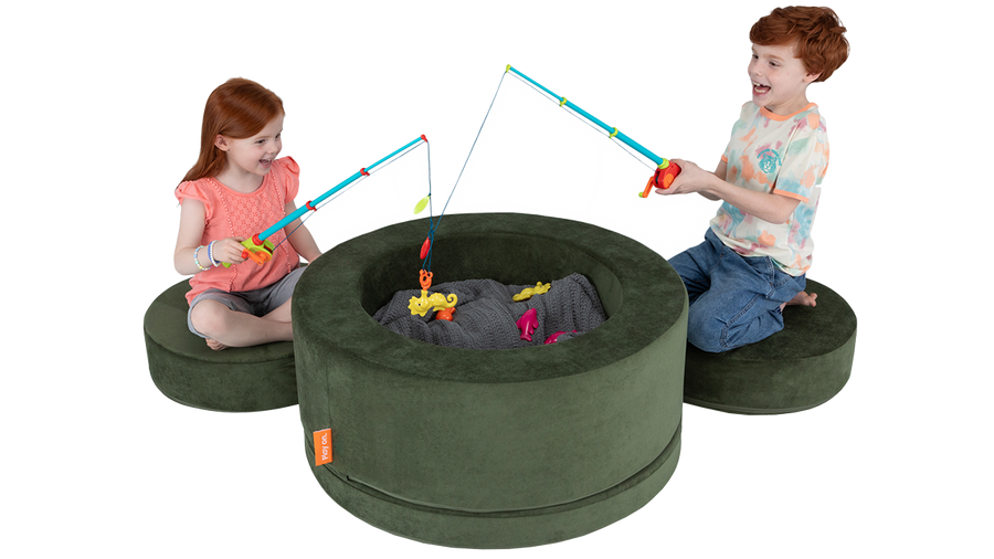 Two children play a magnetic fishing pole game inside a forest green play storage ottoman, using the pieces as seats. 