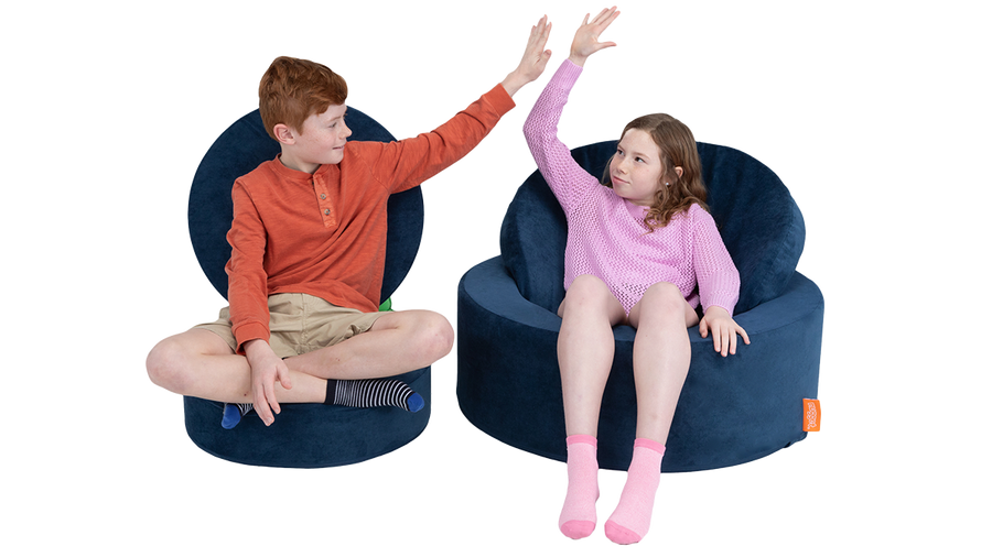 Two children high five from their comfortable playroom seating made from the parts of one navy round play ottoman. 