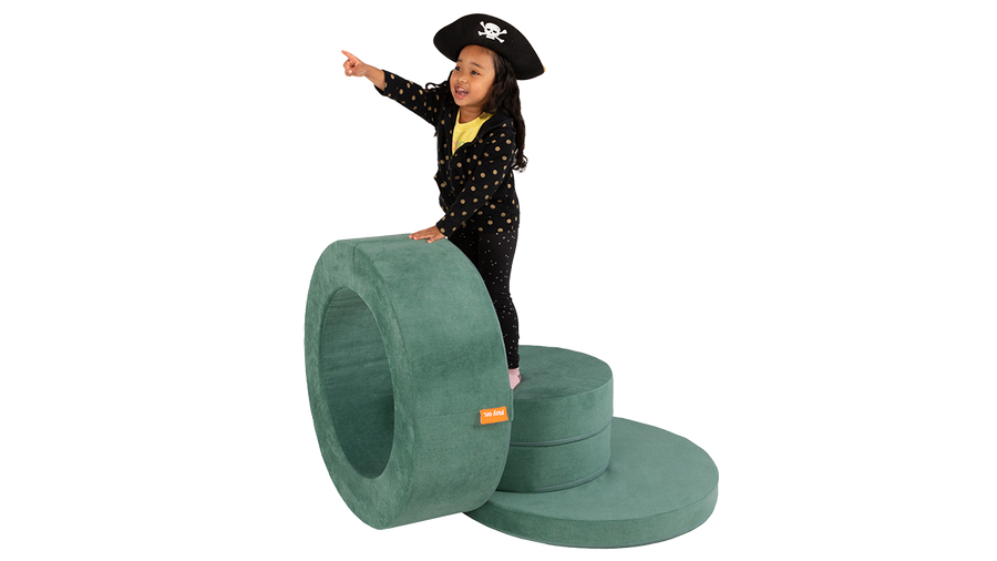 A child plays and pretends to helm the bridge of a pirate ship, built from one sea-green Chunk storage ottoman.