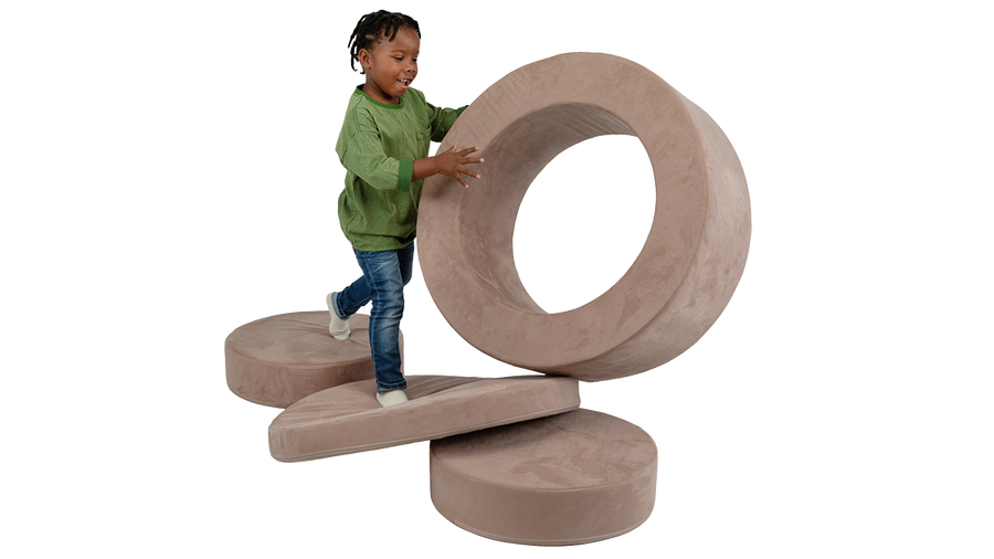 A child plays with the hoop of a Chunk play ottoman, while jumping on the other pieces which are laid out on the ground.