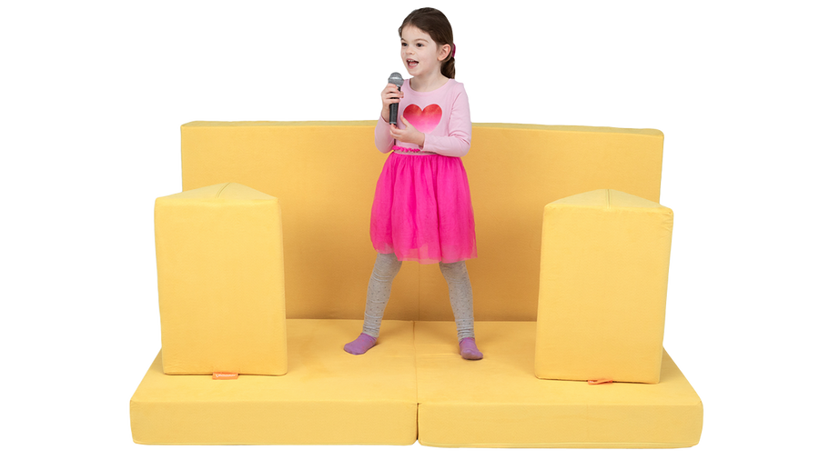 A child talks into a microphone on a one-Nugget stage build, made from a yellow Nugget play couch. 