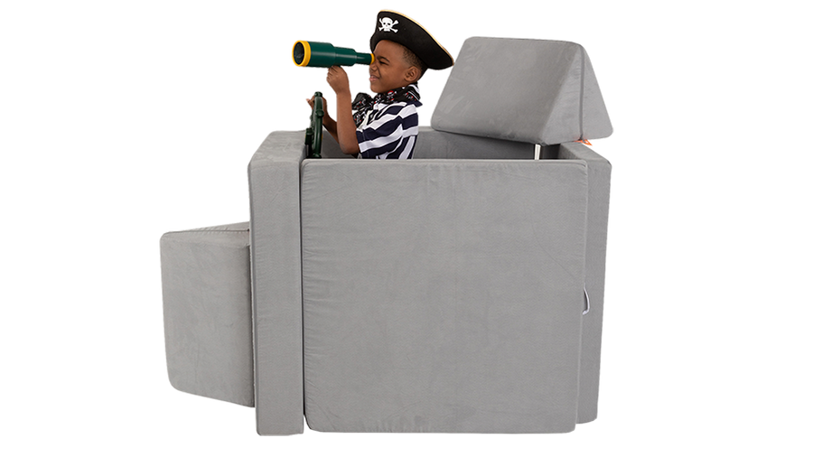 A child looks through a telescope as he plays on a pirate ship build, made from a light gray Nugget play couch.