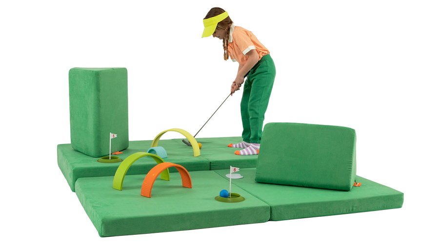 A child plays a round of mini-golf on a course built across a green Nugget play couch.