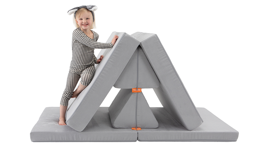 A child smiles and climbs a Nugget mountain build — created using one light gray Nugget play couch.
