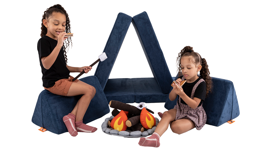 Two children pretend to eat s’mores beside a campsite build, created using a navy blue Nugget play couch.