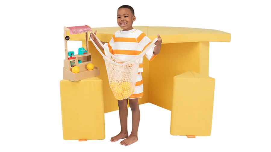 A child pretends to pick out produce at a one-Nugget farmer’s market build, made from a yellow Nugget play couch.