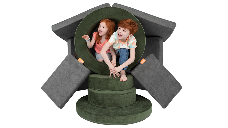 Two kids play around a pretend portal built from Nugget play furniture — one Nugget play couch and one Chunk play ottoman.