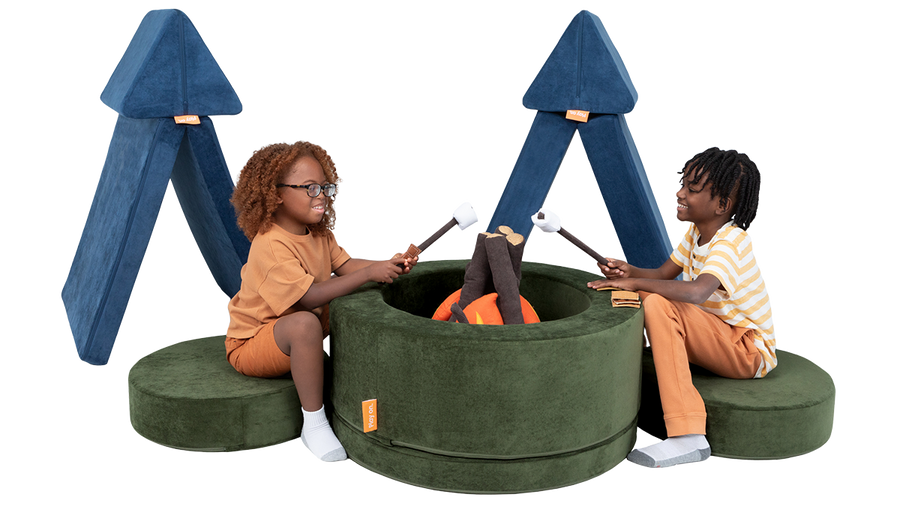 Two children play at a pretend campsite, with tents made out of a Nugget play couch, and a campfire made from a Chunk.