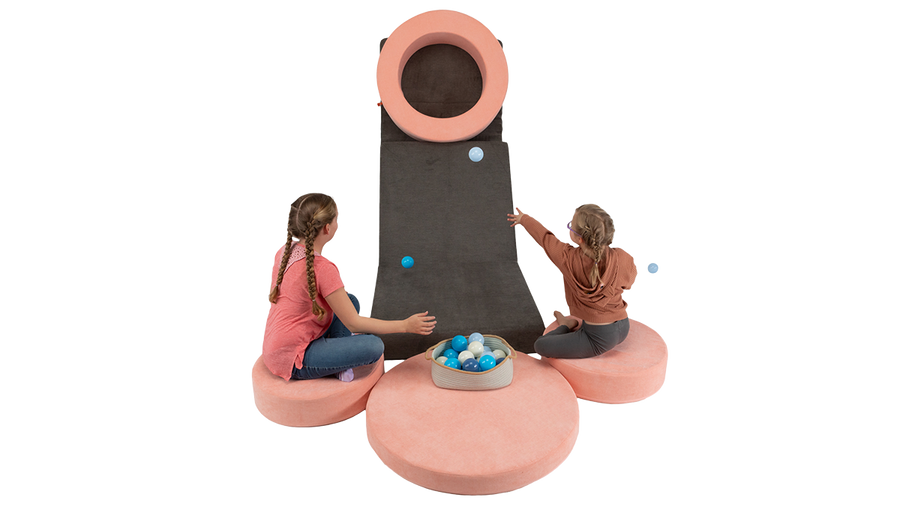 Two kids play a Nuggety version of Skee-ball, using one Nugget play couch as the ramp and a Chunk play ottoman as the target.