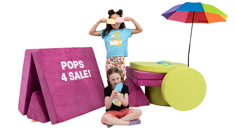 Two kids use a Nugget play couch and a Chunk play ottoman to create an imaginative stand selling popsicles.