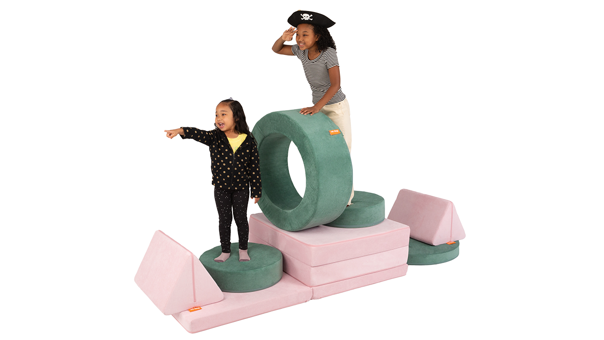 Two kids pretend to sail a play furniture pirate ship, made of a pink Nugget play couch and a sea green Chunk play ottoman.
