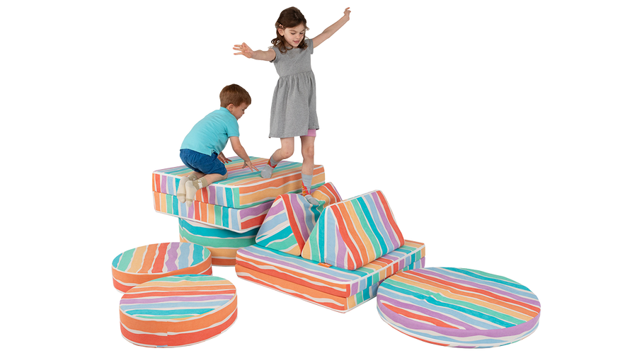 Two children climb around on the pieces of a rainbow-colored Nugget play couch and Chunk play ottoman.