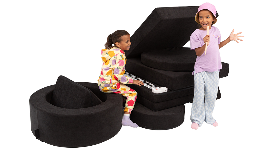 Two children engage in imaginative play with the pieces of a black Nugget play couch and Chunk play ottoman.