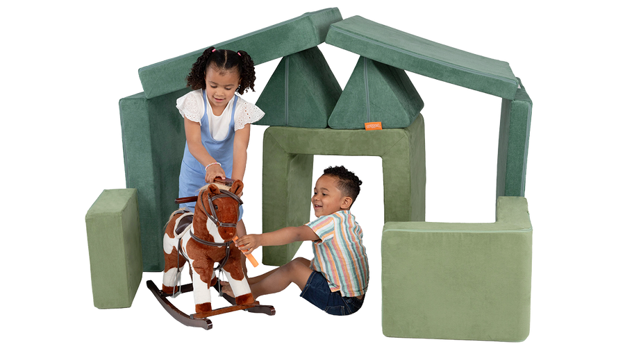 Two children play with a toy pony inside a pretend stable built from the pieces of a Nugget play couch and Smore play chair.