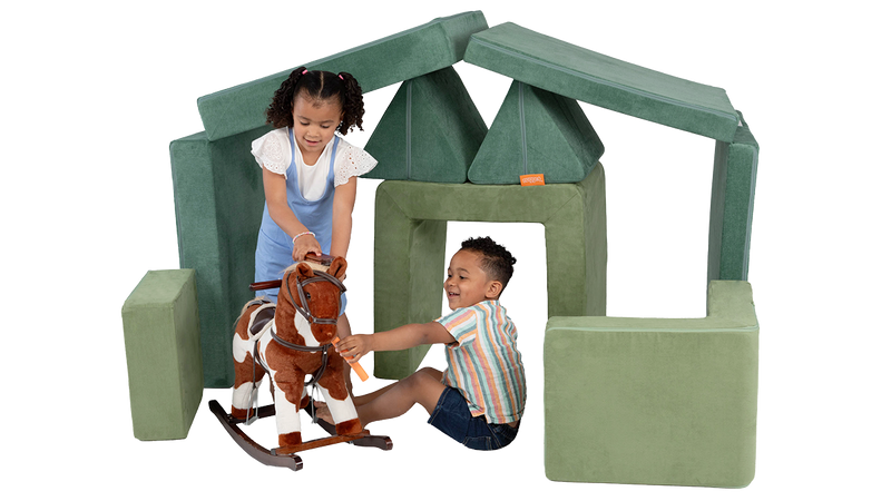 Two children play with a toy pony inside a pretend stable built from the pieces of a Nugget play couch and Smore play chair.