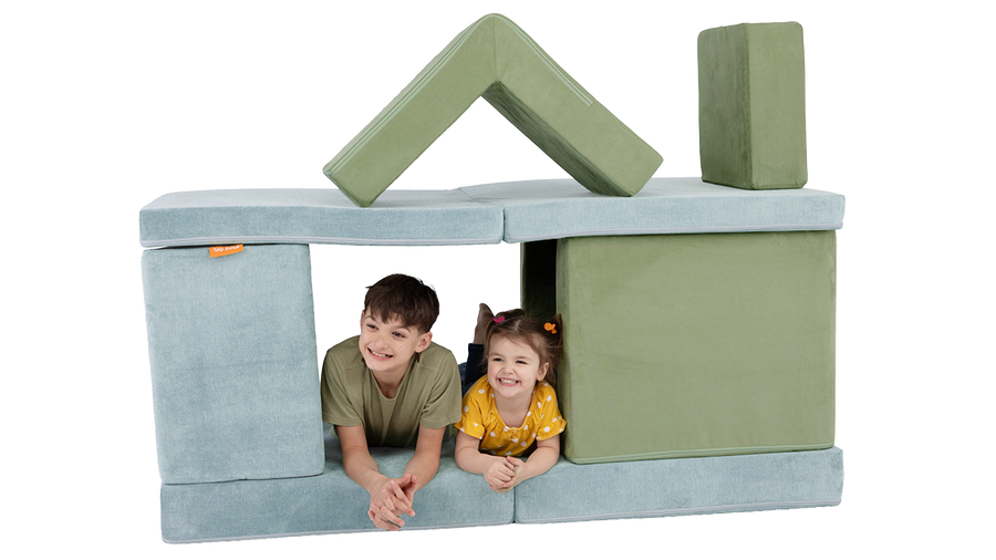 Two children play inside a fort constructed from the pieces of a sage green Smore play chair and blue-gray Nugget play couch.