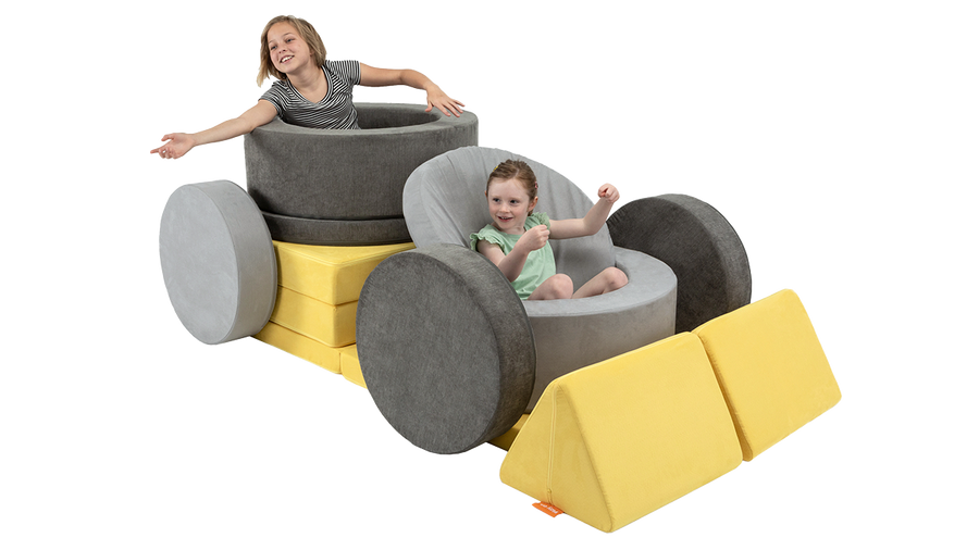 Two children play in a play furniture creation, pretending they’re in a car and waving to their adoring fans. 