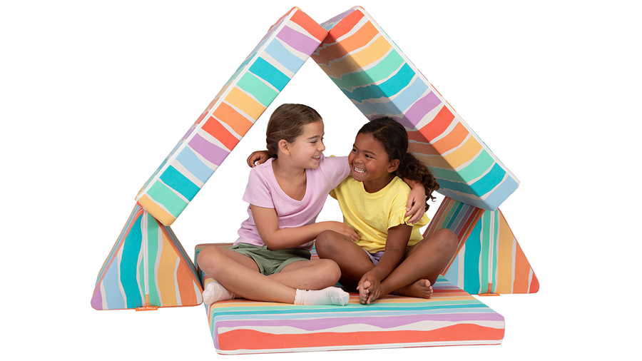 Two children hug and play inside a fort made from a rainbow-colored Nugget play couch.